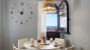A dining area with a round table, white chairs, a clock, and a view through a window. - Apartment "La Estrella" Near Beach with Panoramic Sea View, Terrace, A/C & Wi-Fi (Playa Blanca)