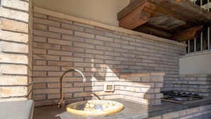 Une cuisine avec un mur de fond en briques, un évier doté d’un robinet ancien et une cuisinière à gaz.