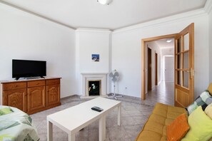 Un salon avec une télévision, un meuble en bois, une table blanche et un canapé avec des coussins.