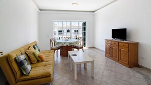 Un salon comprenant un canapé, une table, un téléviseur et un coin repas avec des chaises et une table.