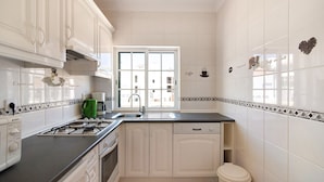 Une cuisine avec des meubles blancs, une cuisinière à gaz, un lave-vaisselle et une fenêtre donnant sur des immeubles.