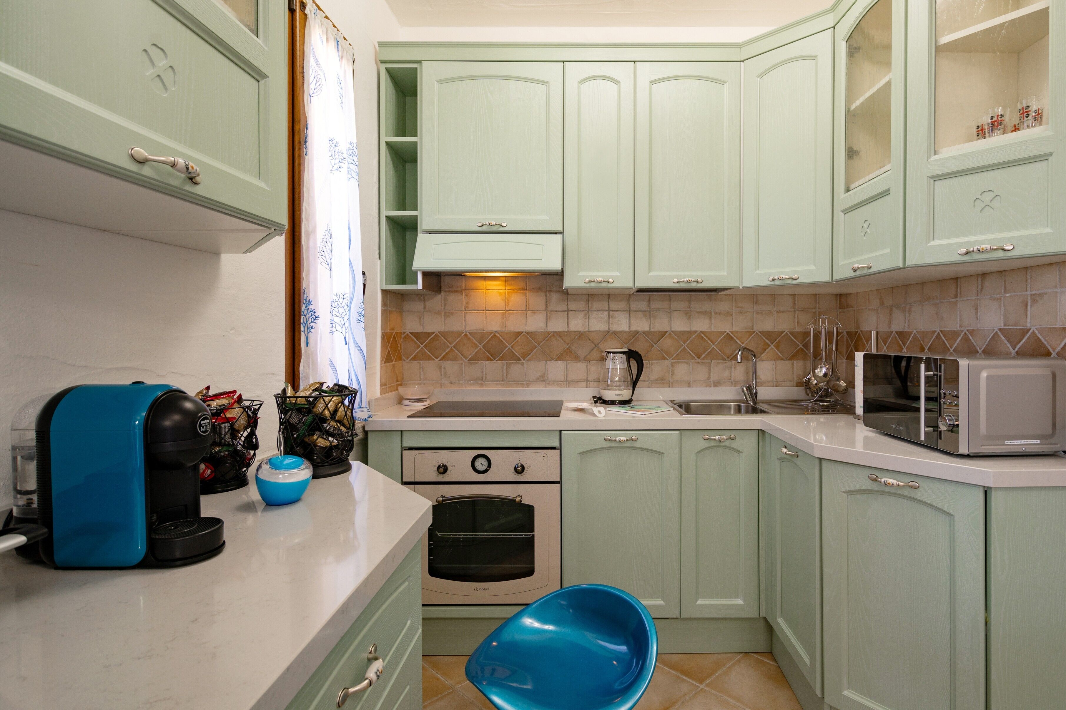 Una cocina con armarios verde claro, un tostador, una tetera y un microondas.