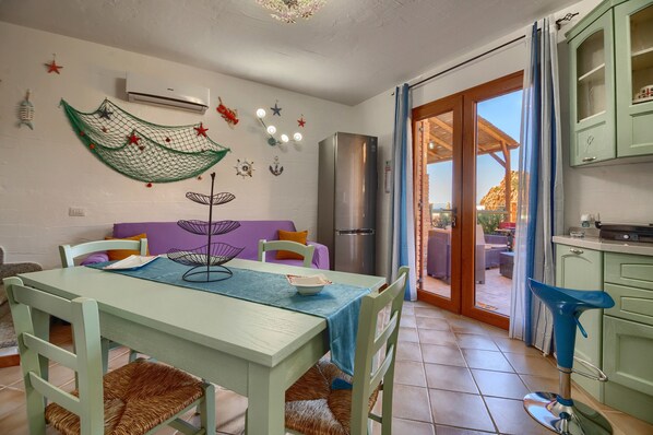 Un comedor con mesa, sillas y una cocina con armarios y refrigerador.