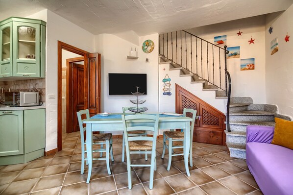 Een eetgedeelte met een tafel en stoelen, een keuken met kasten, een televisie en een trap met decoratieve wandpanelen.