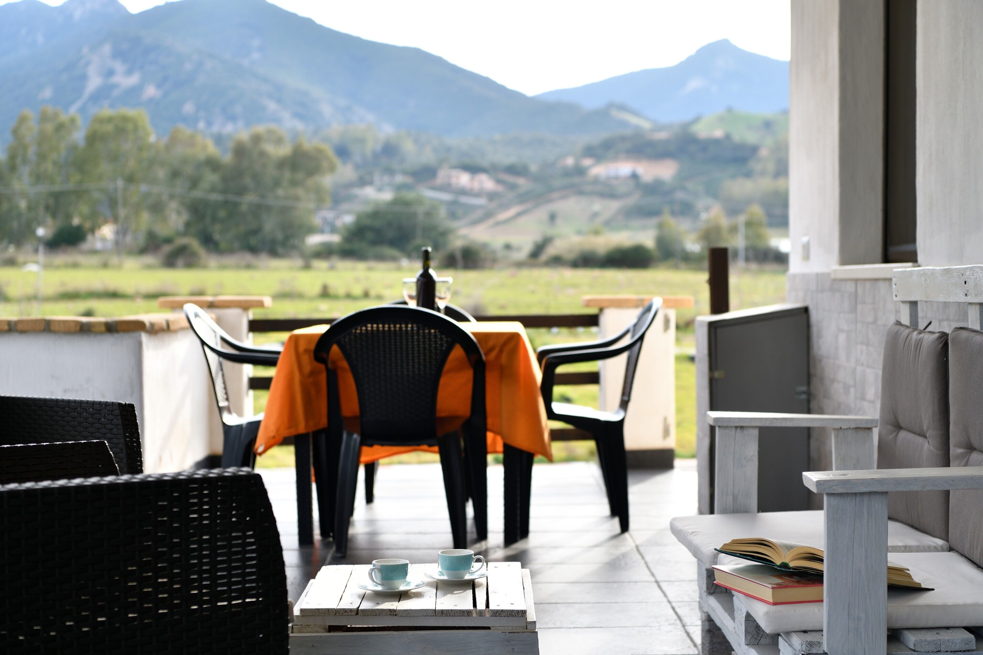 Une terrasse avec des meubles d’extérieur, une table avec des tasses et un livre, et une vue sur les montagnes.