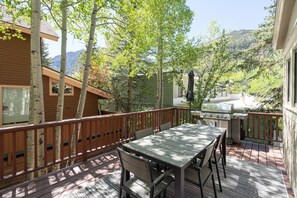 A deck with a table and chairs, a grill, and a view of mountains.