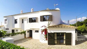 A white two-story house with a stone-paved courtyard, a small attached structure with a tiled roof, and a white picket fence. - Villa Coelho with Sea View, Pool, Garden & Wi-Fi (Albufeira)