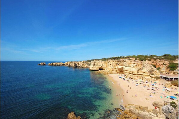 Una playa costera con aguas transparentes, acantilados rocosos y una orilla arenosa con sombrillas.