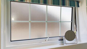 A window with frosted glass panes, a curtain, and a round mirror on a white sill. - Foxes Lair  Holiday Home Looe Cornwall (Looe)