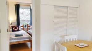 A room with two beds, a wooden table, white chairs, a window with curtains, and a white radiator. - Foxes Lair  Holiday Home Looe Cornwall (Looe)