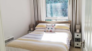 Una cama bien hecha con ropa de cama a rayas, un cojín estampado con motivos de estrellas y una mesita de noche con lámpara.