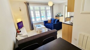 Un espacio habitable compacto con comedor, sofá, televisión y área de cocina.