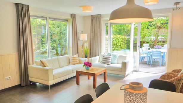 A modern living room with a sofa, coffee table, and dining area. - Duinland 49a Holiday home Sint Maartenszee (Sint Maartensvlotbrug)