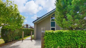 A modern house with a paved driveway, a wooden gate, and a well-maintained hedge. - Duinland 49a Holiday home Sint Maartenszee (Sint Maartensvlotbrug)