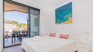 A bedroom with a bed, a nightstand, a painting, and a view of the outside. - MIRADOR BLUE G   Ref: CS20 (Cala Sant Vicenç)