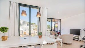 A modern living room with a white table, two chairs, a sofa, a TV, and a balcony with a view of buildings. - MIRADOR BLUE G   Ref: CS20 (Cala Sant Vicenç)