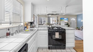 Une cuisine moderne avec des meubles blancs, une cuisinière noire et une grande fenêtre.