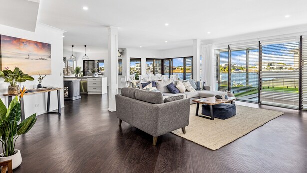 A modern living room with a grey sofa, a dining area, and a kitchen.