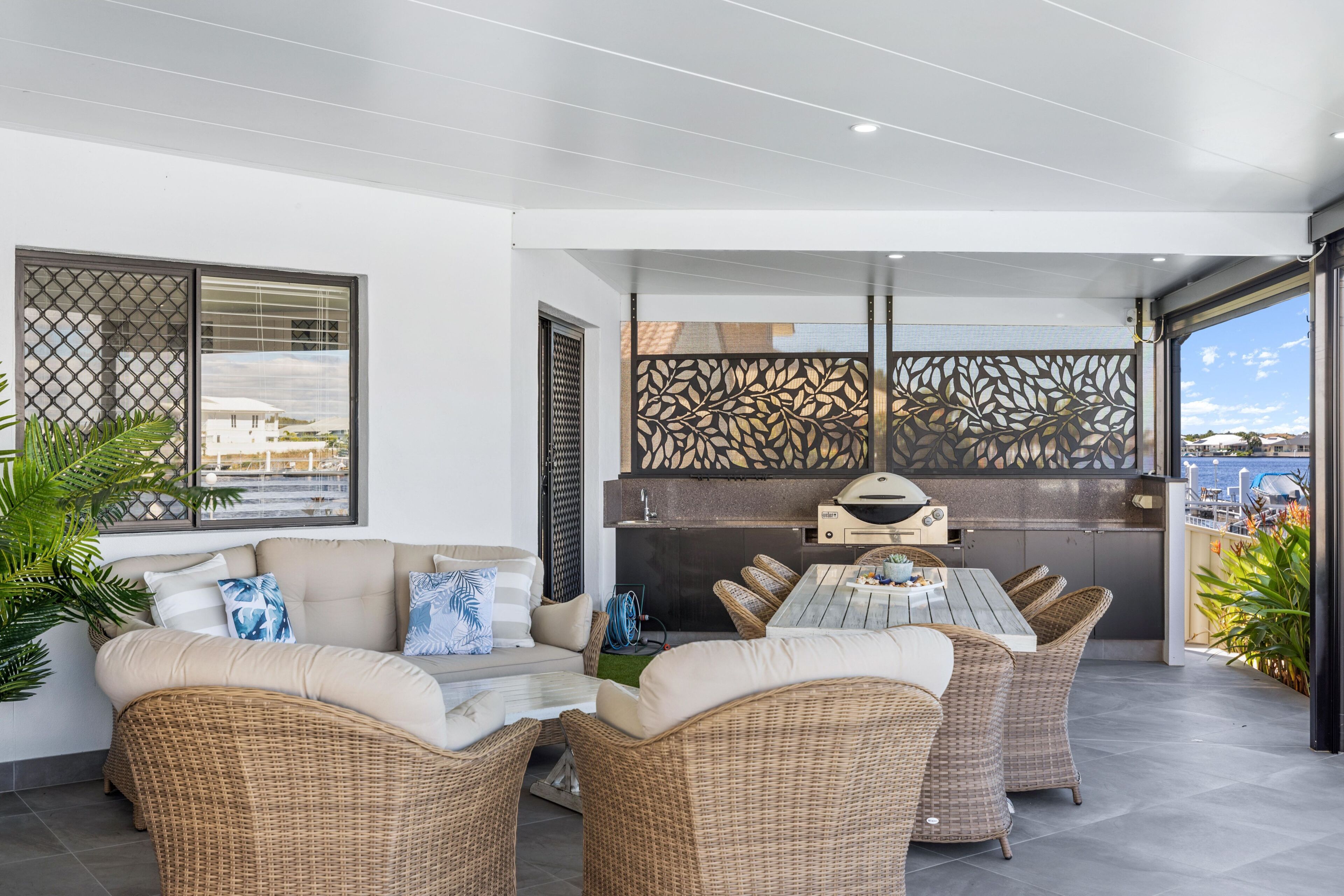 A modern outdoor patio with wicker furniture, a grill, and a view of the sea.