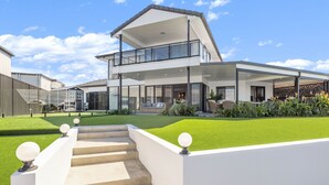 A modern two-story house with a balcony, a well-maintained lawn, and a staircase leading to the entrance.