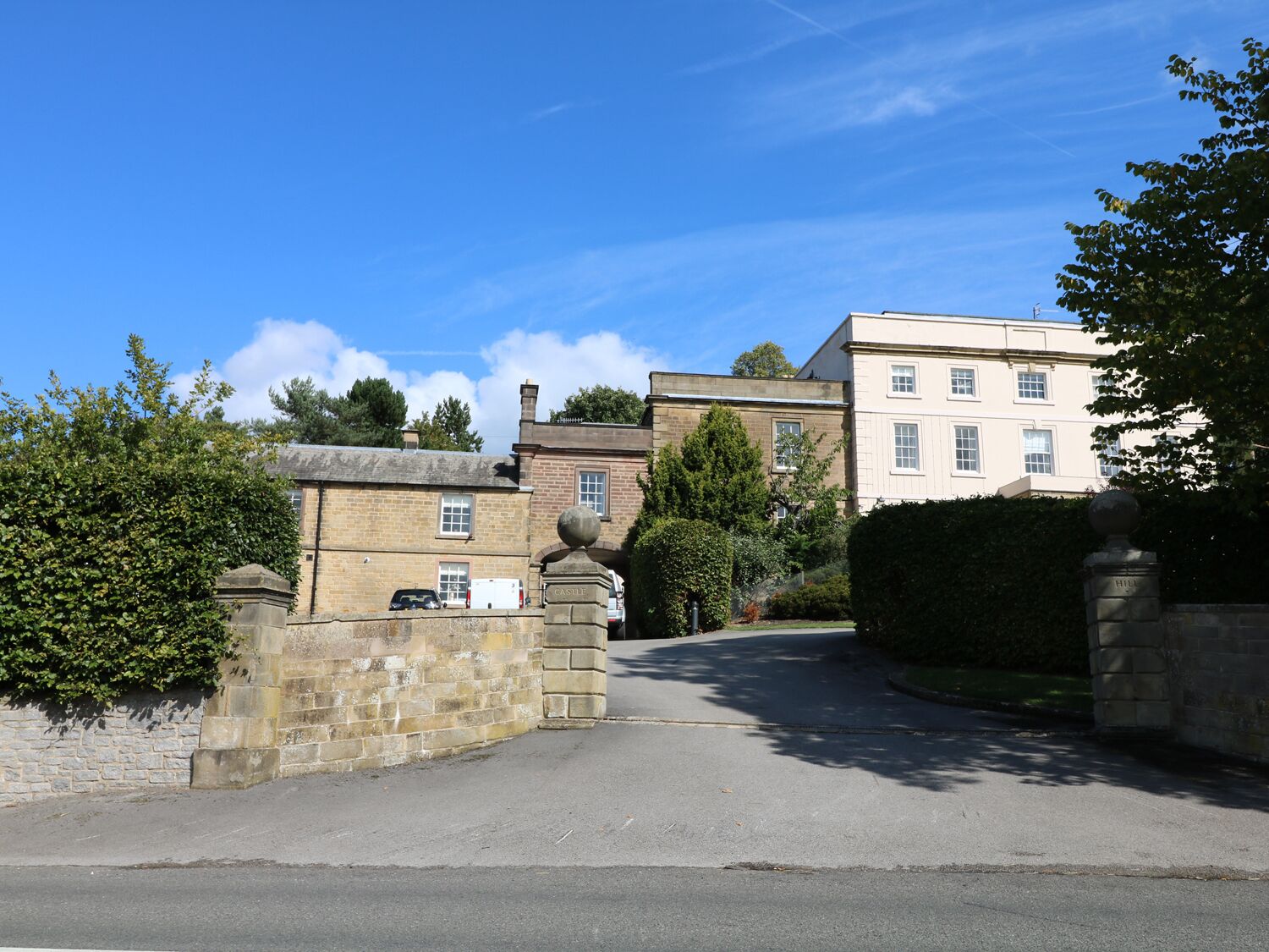 A traditional stone building with a gated entrance, a paved driveway, and a clear blue sky.