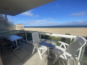A balcony with a table and chairs, overlooking a beach.