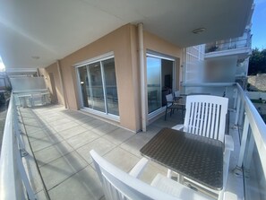 A balcony with a table and chairs, a sliding glass door, and a view of a building across the street.