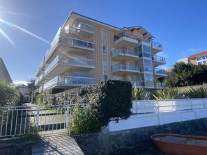 A multi-story residential building with balconies, a gated entrance, and a stone wall.