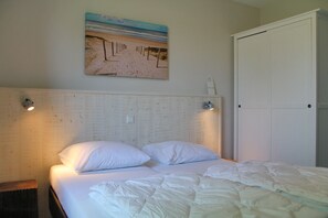 Une chambre à coucher avec un lit, du linge de lit blanc, une tête de lit, un tableau accroché au mur et une porte.