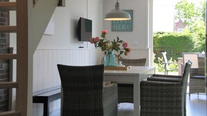 Zona pranzo con sedie in vimini, un tavolo con un vaso di fiori, un lampadario e un televisore a parete.