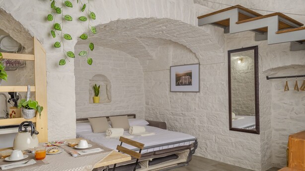 Um quarto aconchegante com uma cama, uma mesa com itens de café da manhã, um espelho e uma planta pendente.