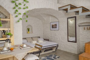 Una habitación acogedora con una cama, una mesa con alimentos para el desayuno, un espejo y una planta colgante.