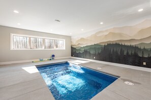 Una piscina con un mural de montañas en la pared, una ventana con persianas y un techo con iluminación empotrada.