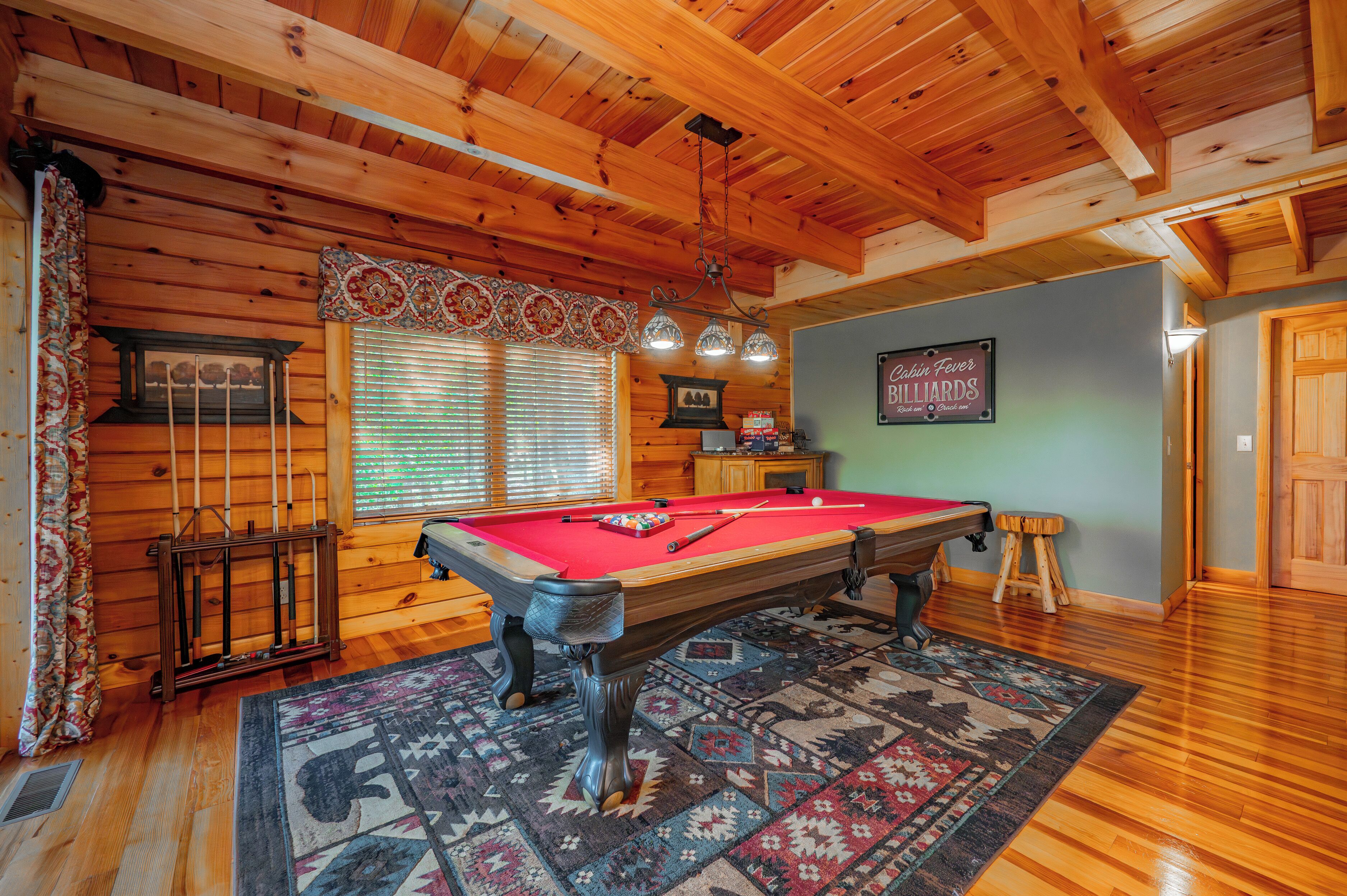 A pool table in a room with wooden walls and a ceiling with exposed beams.