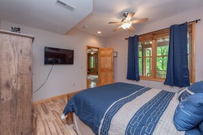 Un dormitorio con cama, suelo de madera, ventilador de techo, televisor y vistas al exterior a través de una ventana.