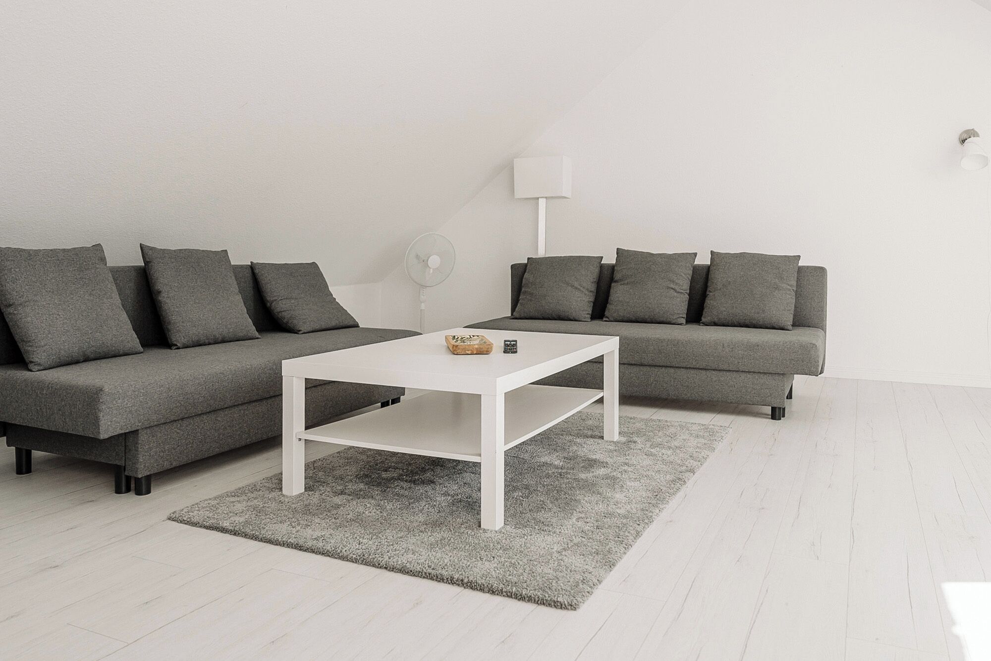 Een moderne woonkamer met twee grijze banken, een witte salontafel en een grijs vloerkleed.
