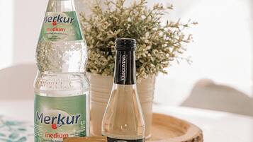 Una botella de agua mineral Merkur mediana, una botella de Secco Frizzante y una barra de caramelos Haribo sobre una mesa con mantel floreado.
