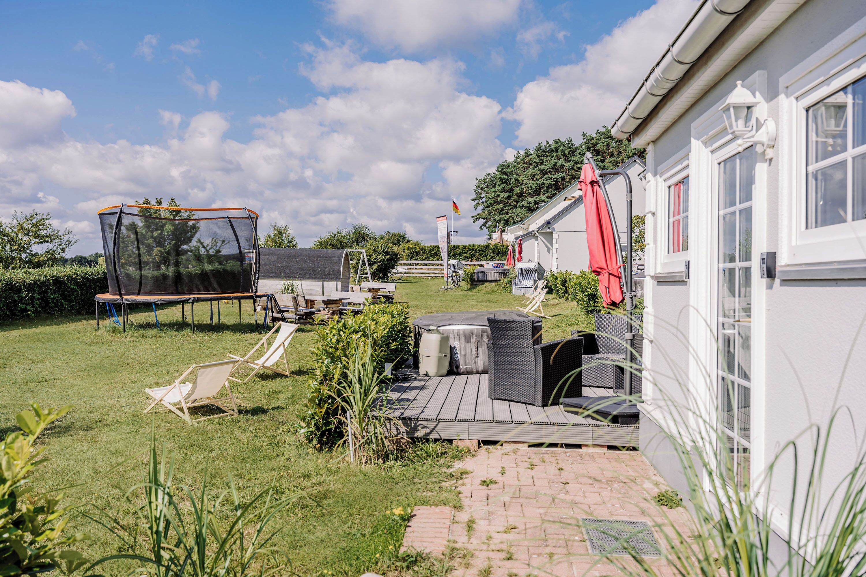 Un jardin avec un trampoline, un coin salon extérieur et une maison dotée d’un auvent rouge.