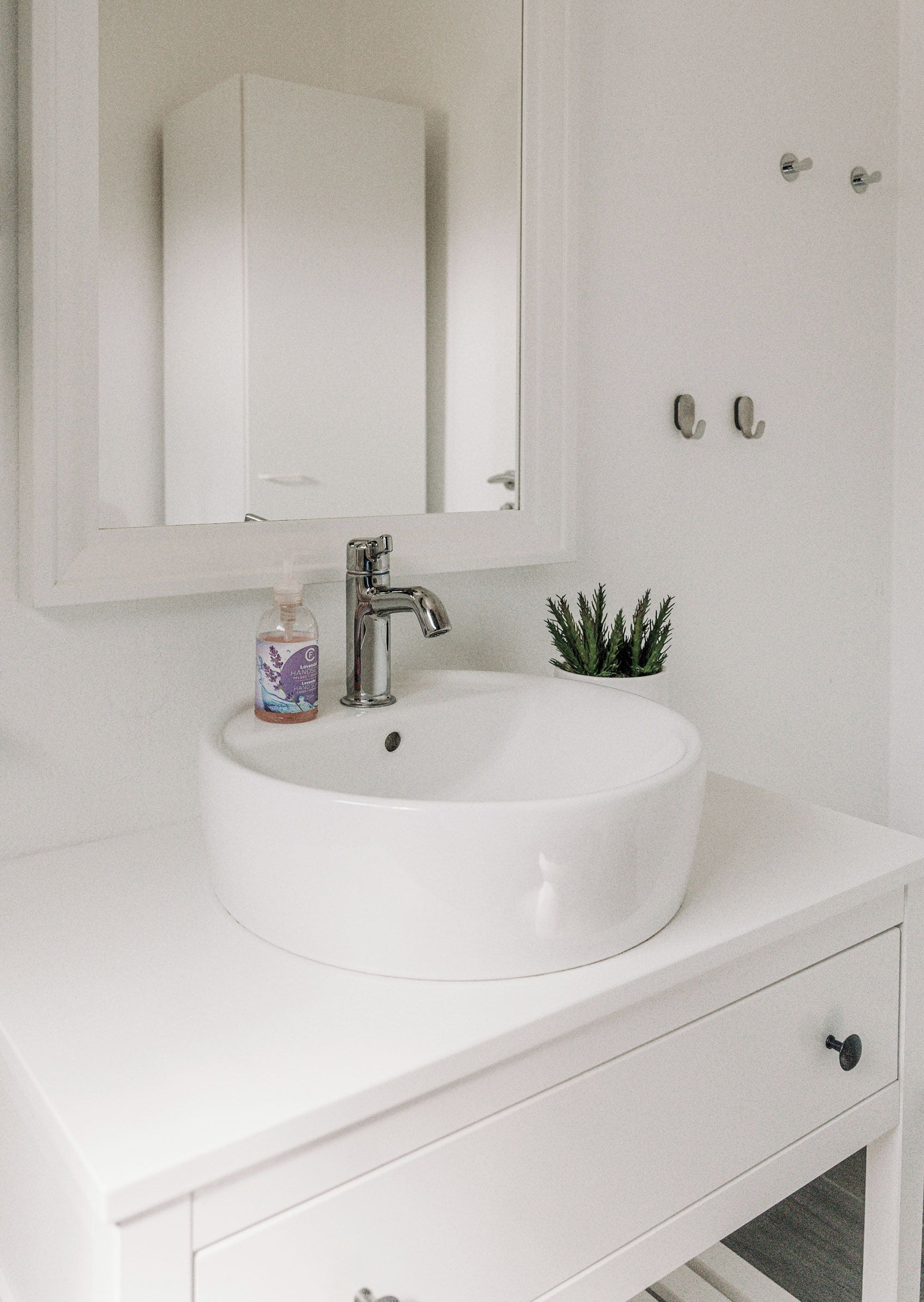Un tocador blanco con un lavabo redondo, un espejo encima y una pequeña planta en maceta al lado del lavabo.