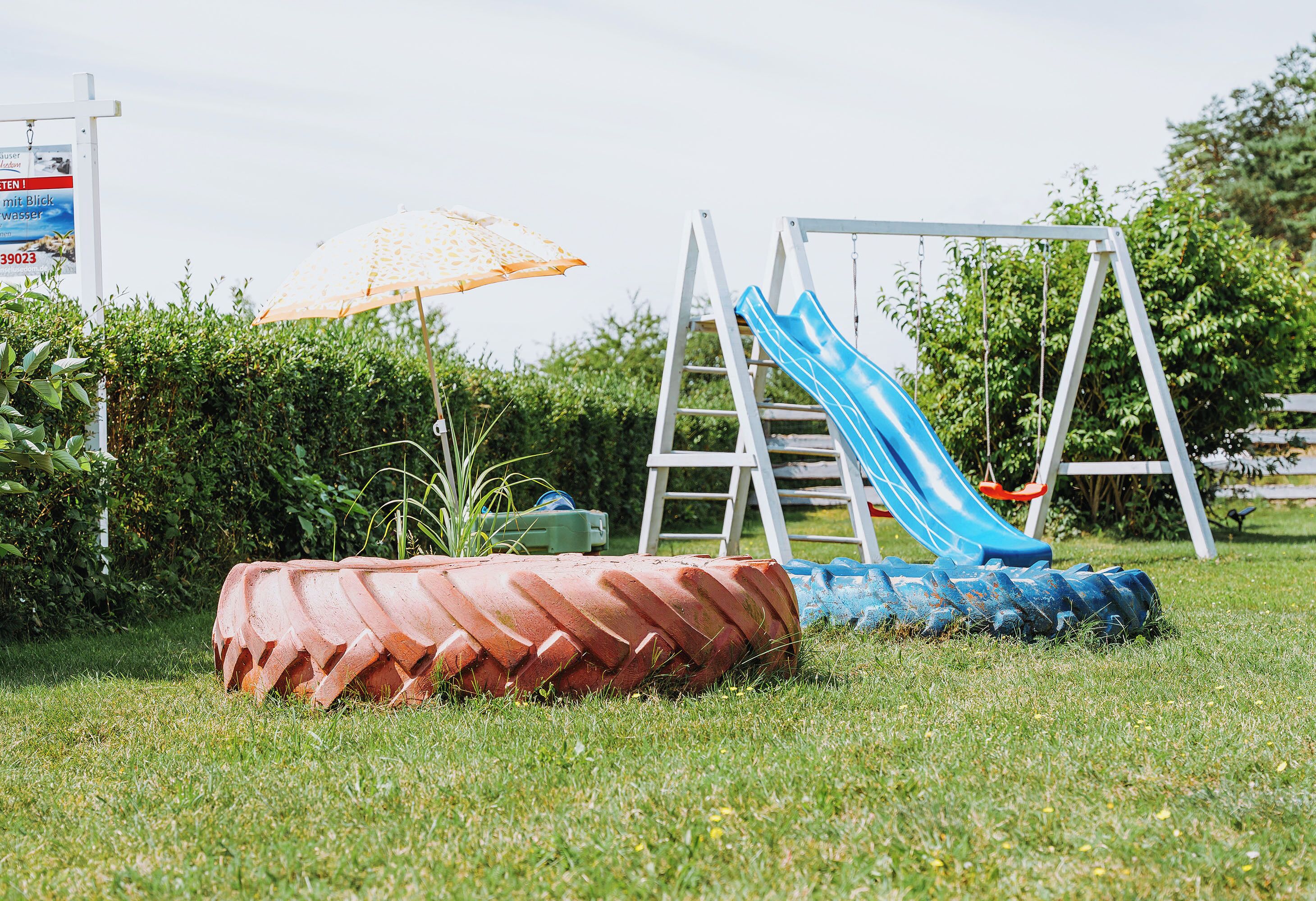 A playground with a slide and swing set, surrounded by grass and greenery.