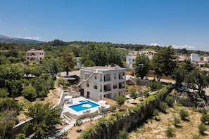 Um edifício moderno de dois andares com piscina, cercado por árvores e outros edifícios residenciais.