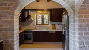 A kitchen with a stone archway, wooden cabinets, a stainless steel refrigerator, and a window with a view of greenery.