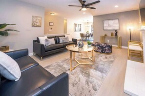 A modern living room with a sofa, a round coffee table, and a dining area in the background.