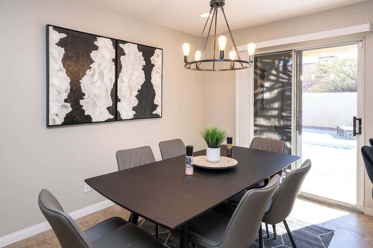 A dining area with a dark wooden table, six chairs, a chandelier, a potted plant, and a large abstract painting on the wall.