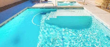 A swimming pool with clear water, a diving board, and lounge chairs.