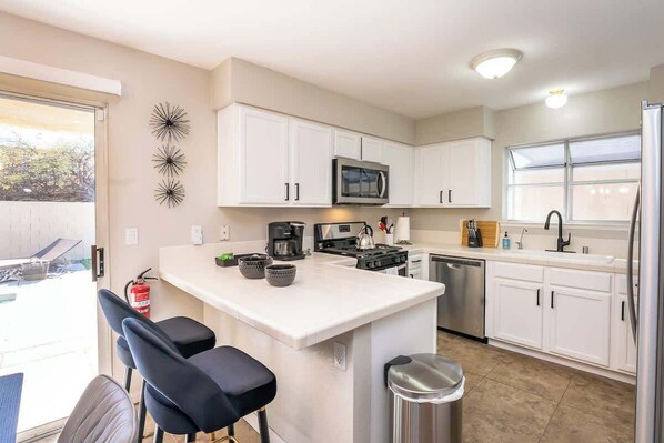 A modern kitchen with white cabinets, a central island with bar stools, a microwave, stove, and dishwasher.