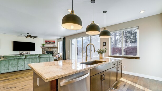 Una cocina moderna con una isla central, electrodomésticos de acero inoxidable, iluminación colgante y un amplio ventanal que proporciona luz natural.