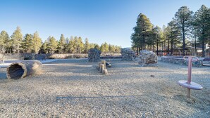 Un parque infantil con formaciones rocosas naturales, un tronco grande y columpios.