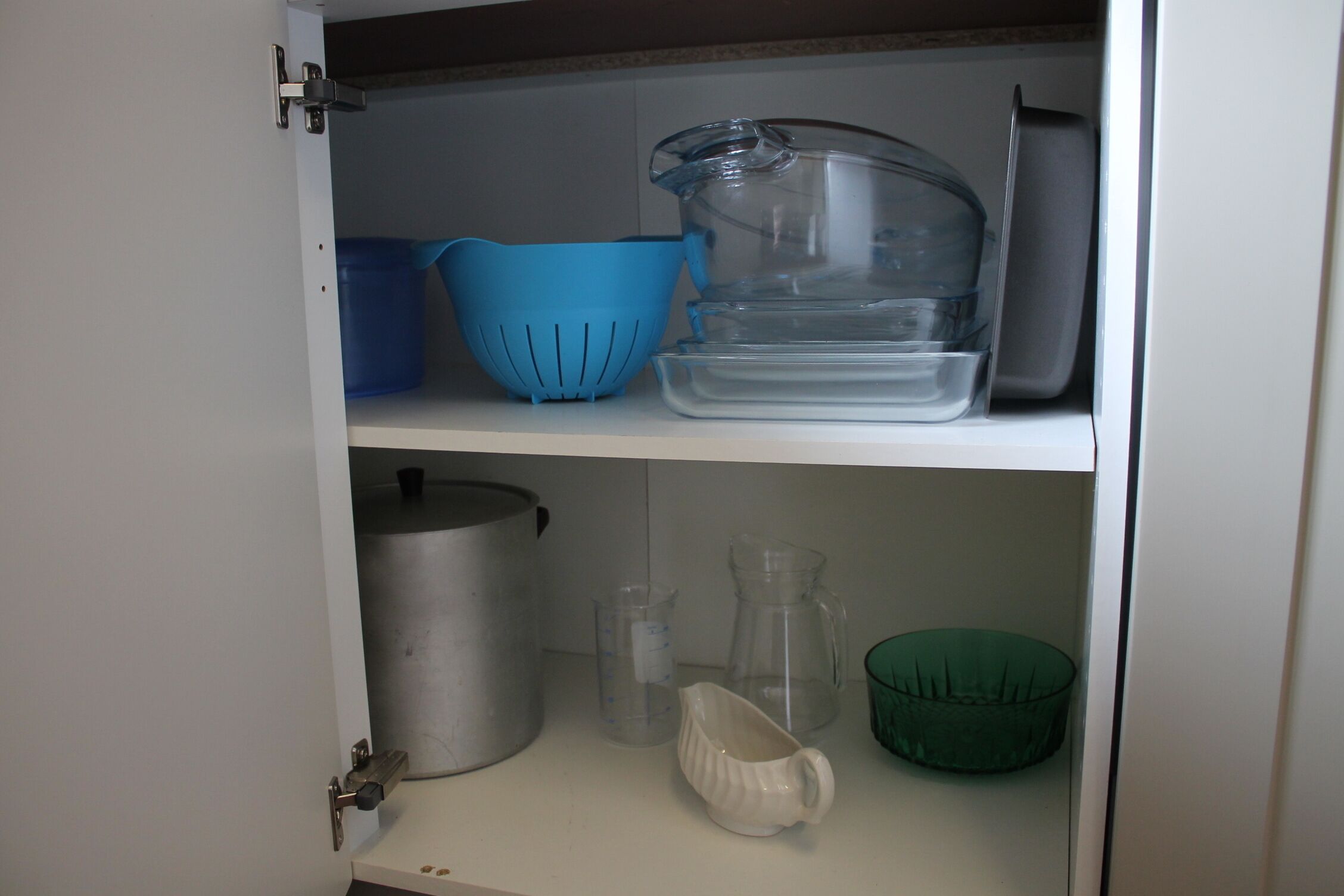 Un meuble de cuisine contenant divers ustensiles et récipients, notamment une passoire bleue, un pichet transparent et un saladier vert.