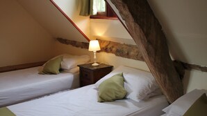 Ein gemütliches Schlafzimmer im Dachgeschoss mit zwei Einzelbetten, einem Nachttisch mit Lampe und einer geneigten Decke.